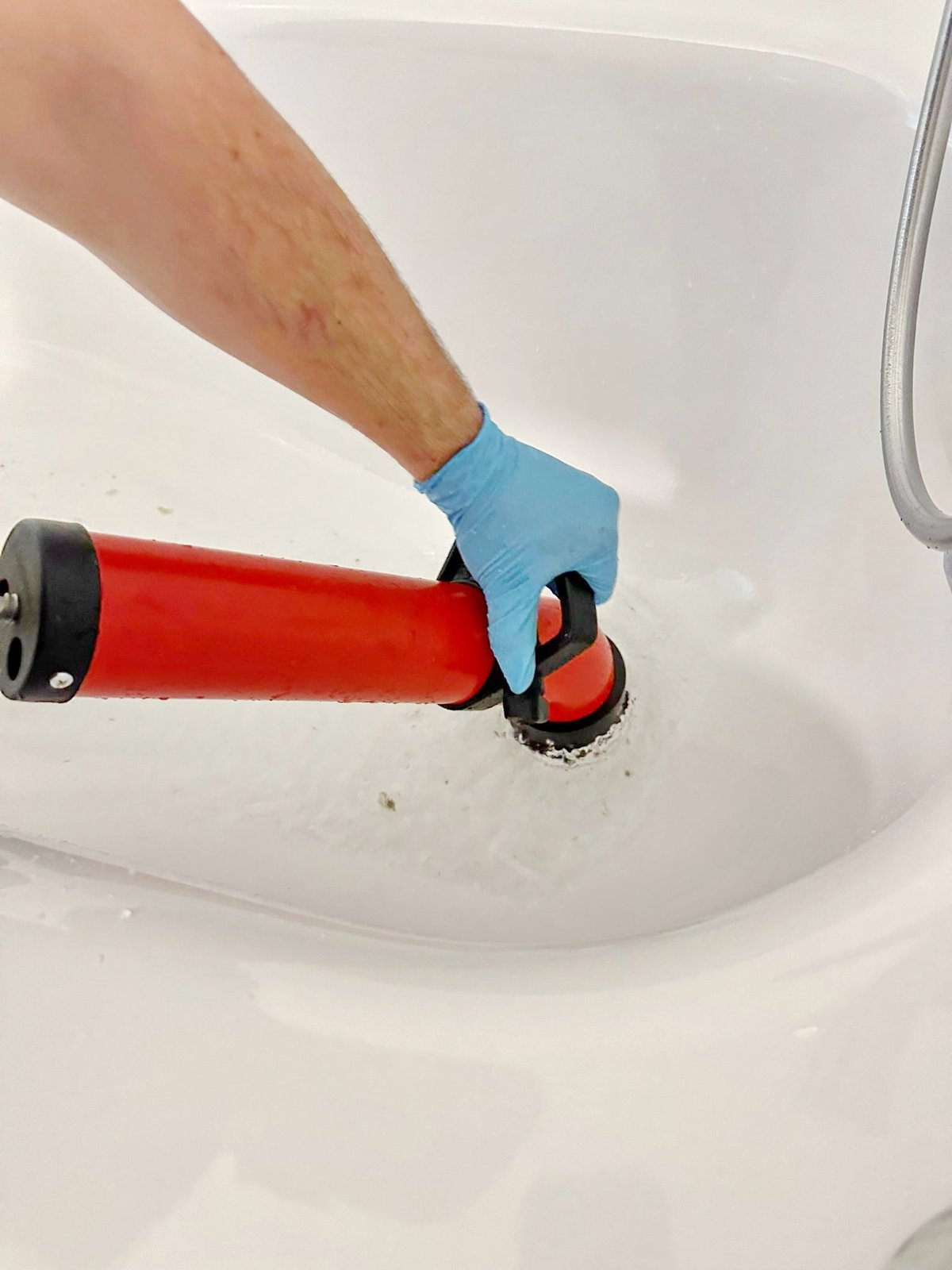 Rote Absaugpumpe an Toiletten-Abfluss, blaue Gummihandschuhe